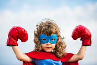 Girl dressed as superhero in red cape raises boxing gloves like a champion